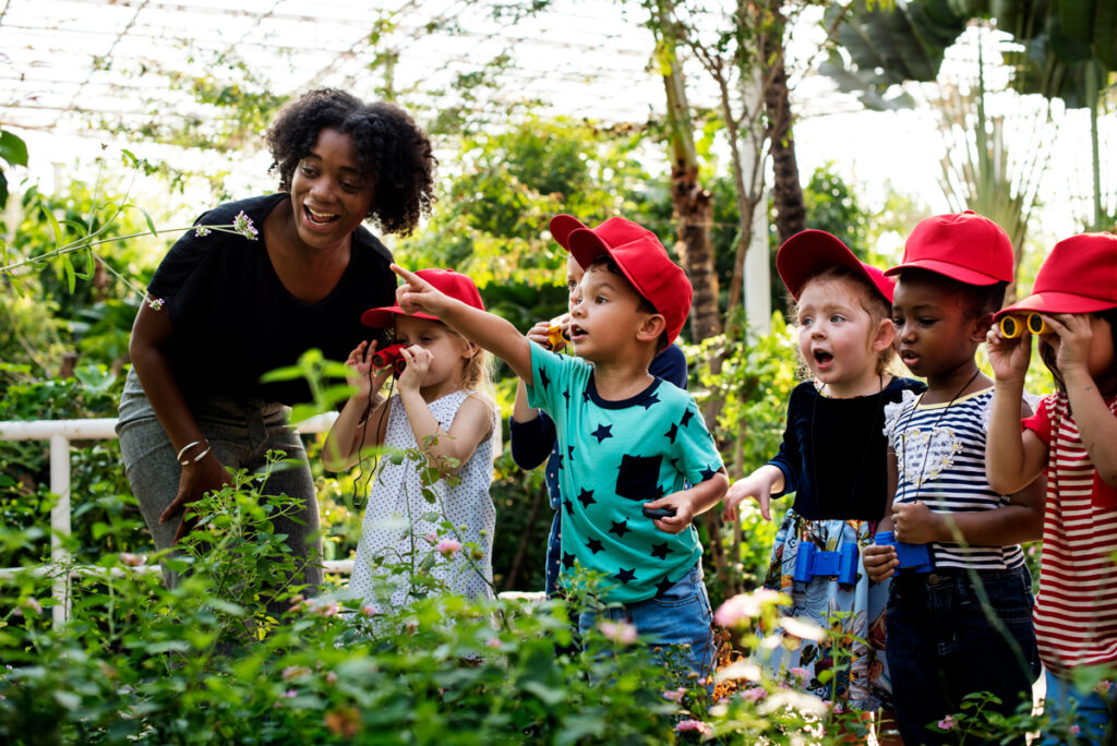 Group of children in red hats enjoying nature in a garden.