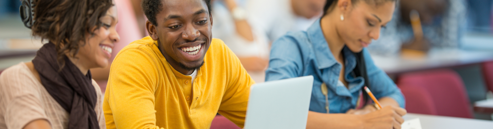 students smiling in class, yellow long sleeve shirt, happy, writing, focused on work, workshop, helping, study