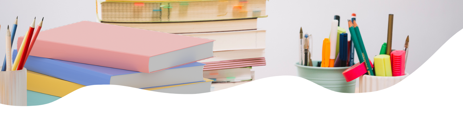 Stack of pastel-colored books with pencils and pens in containers on a desk.